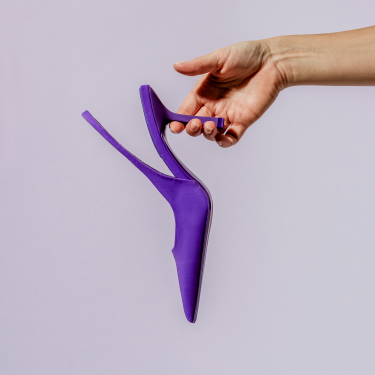 Purple velvet high heeled pump being held on a lavender background